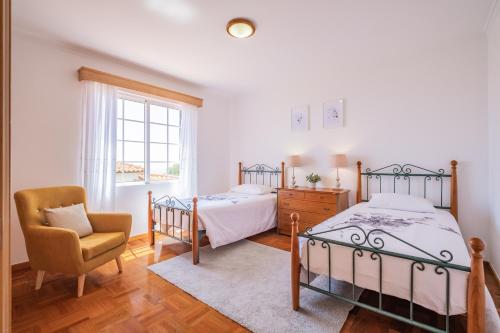 a bedroom with two beds and a chair and a window at Casa Flor do Campo in Calheta