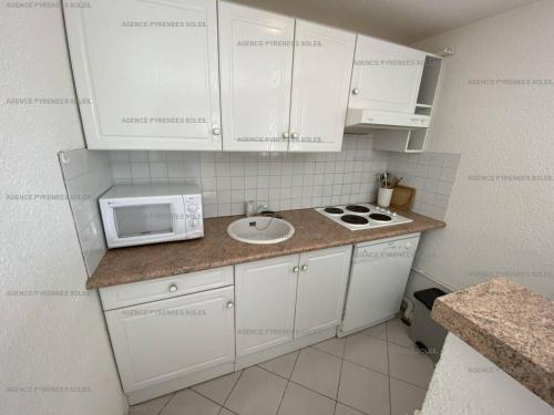 une petite cuisine avec des armoires blanches et un micro-ondes dans l'établissement Appartement F3 avec Wi-Fi, parking et terrasse - 6 couchages, proche centre et navette gratuite - FR-1-295-157, aux Angles