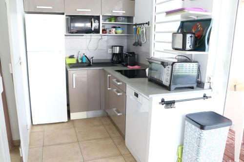 a small kitchen with white cabinets and a microwave at Bungalow colombo résidence Ti-Figues in Saint-François