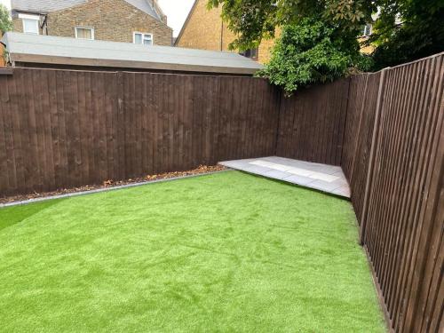 un patio trasero con una valla y un césped verde en London flat with garden, en Catford