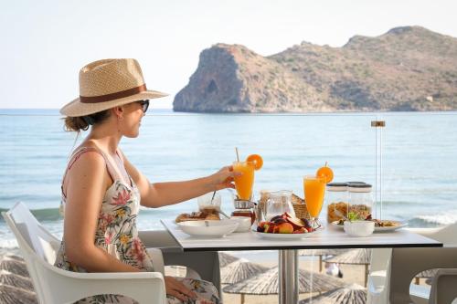 a woman sitting at a table with a meal on the beach at Vergina Beach Hotel in Agia Marina Nea Kydonias