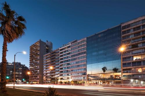a large building with a palm tree in front of a street at Hotel Costanero MGallery - ACCOR in Montevideo