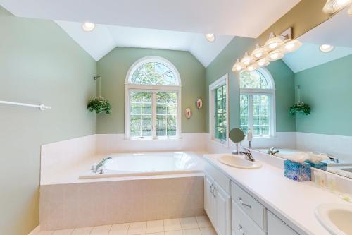 a bathroom with a tub and two sinks and two mirrors at Spinnaker Trail in Orleans