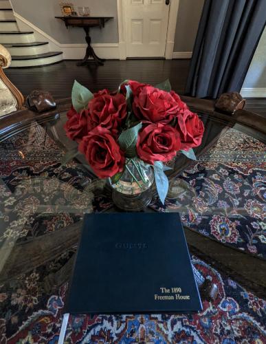 a vase of red roses on a table with a book at The 1890 Freeman House in Galveston