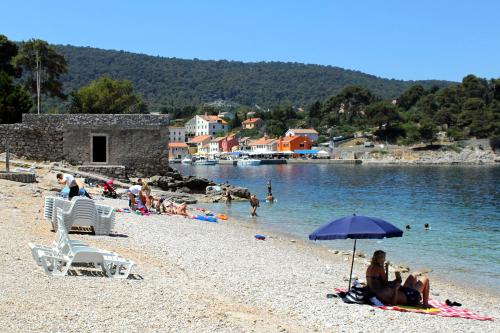 a group of people sitting on a beach with an umbrella at Apartments with a parking space Veli Losinj, Losinj - 8060 in Veli Lošinj