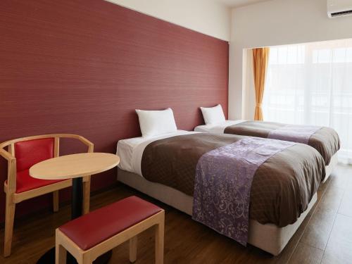 una camera d'albergo con due letti e un tavolo con sedia di ミチ旅ホテル 読谷 a Yomitan