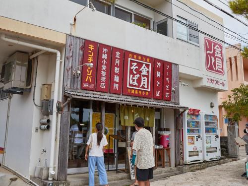 two people are standing outside of a building at ミチ旅ホテル 読谷 in Yomitan