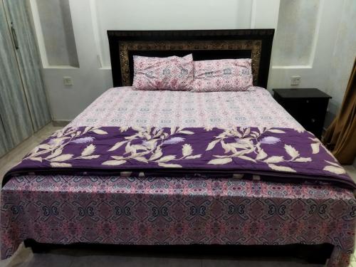 a bed with a purple comforter and pillows on it at Furnished Private Ground Floor - Pasha House in Lahore