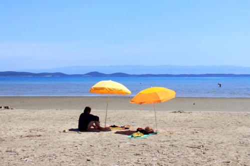 2 personnes assises sous des parasols jaunes sur une plage dans l'établissement Apartments by the sea Susak, Losinj - 14713, à Susak