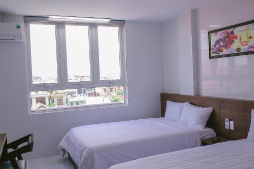 a hotel room with two beds and two windows at Vagibi Hotel in Dong Hoi