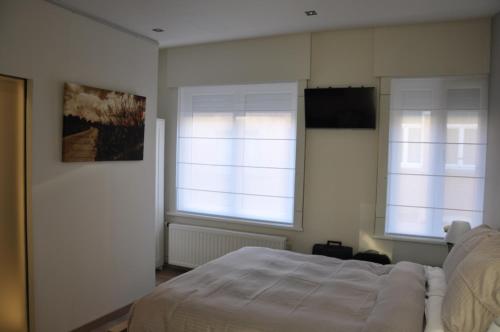 a bedroom with a white bed and two windows at Het Houten Paard in Ypres