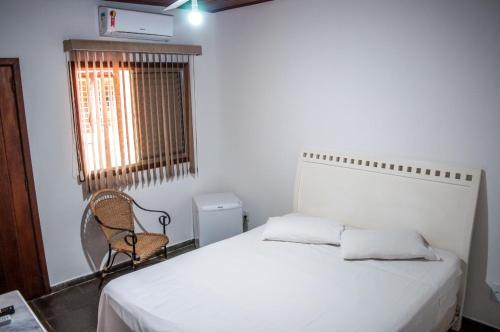 a bedroom with a bed and a chair and a window at Galeria Hotel Pousada in Jaguariúna