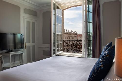 a bedroom with a large bed and a large window at Grand Hotel De La Reine - Place Stanislas in Nancy