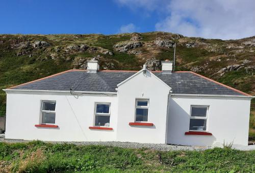 a white house with a mountain in the background at Conneelys Cottage, Connemara, Clifden, H71Y096 in Clifden