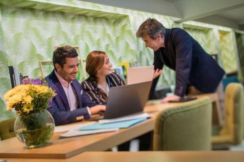 three people sitting at a table looking at a laptop at Apartosuites Jardines de Sabatini in Madrid