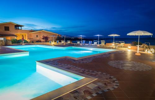 una piscina por la noche con sombrillas en Appartamenti Marineledda Golfo di Marinella, en Golfo Aranci