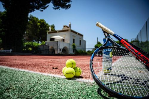 Tre palle da tennis sedute su un campo da tennis con racchetta di Antica Casina B&B di Charme a Pulsano