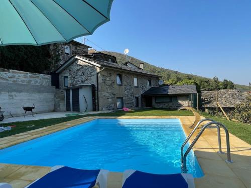 a swimming pool in front of a house with an umbrella at Recantos da Montanha in Candal