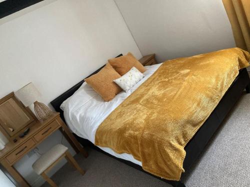 a bedroom with a bed with a gold blanket and a table at Cragside Cottage in Troutbeck
