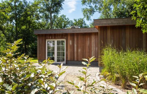 a small wooden shed with a door in a garden at Het Spechtennest in Zedelgem