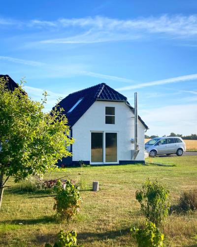 a white house with a car parked in a field at Hyggehytten auf Bornholm in Østermarie