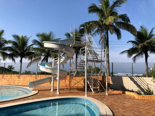 a water slide next to a swimming pool with palm trees at Apartamento beira mar - Praia de Boraceia in Bertioga
