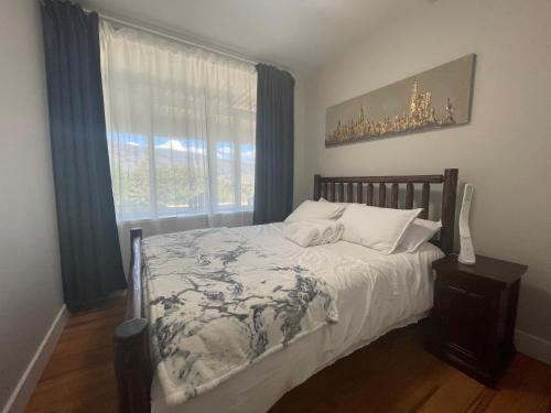 Kaleden Guest Suite في Okanagan Falls: غرفة نوم بسرير وملاءات بيضاء ونافذة