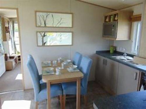 a kitchen with a wooden table and blue chairs at Roxbury 5 Star 6 berth Luxury Caravan in Exeter