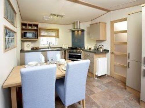 a kitchen with a wooden table and white chairs at Roxbury 5 Star 6 berth Luxury Caravan in Exeter