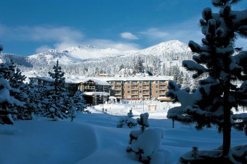 a hotel in the snow with mountains in the background at Juniper Springs Resort in Mammoth Lakes