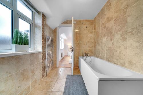 La salle de bains est pourvue d'une baignoire et d'une fenêtre. dans l'établissement Modern Deluxe 5 Bed 3 Bath House London Camberwell Denmark Private Parking, à Londres
