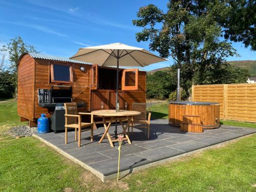 um pátio com um guarda-sol, uma mesa e cadeiras em Vale View Glamping em Ruthin