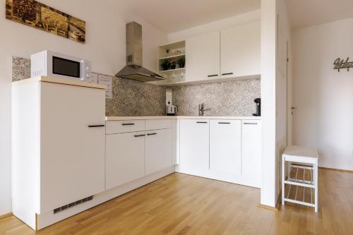 a white kitchen with white cabinets and a wooden floor at Vienna City and SPA - Modern Apartments next to Therme Wien & 15 Minutes to the City Center in Vienna