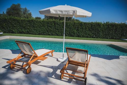 2 sillas y sombrilla junto a la piscina en Dimorae Camà en Cisternino