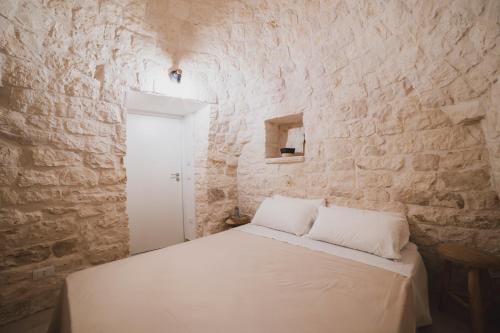 a bedroom with a white bed in a stone wall at Dimorae Camà in Cisternino