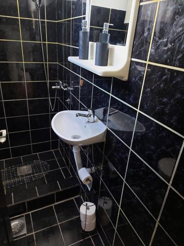 Baño de azulejos negros con lavabo y espejo en Kuća na dan en Šid