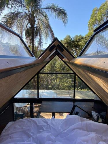 a bed in a tent with a view of a palm tree at Toca do Pica-Pau - Tiny House em Campos com Lareira e privacidade! in Campos do Jordão
