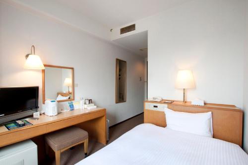 a hotel room with a bed and a desk with a mirror at Smile Hotel Sugamo in Tokyo