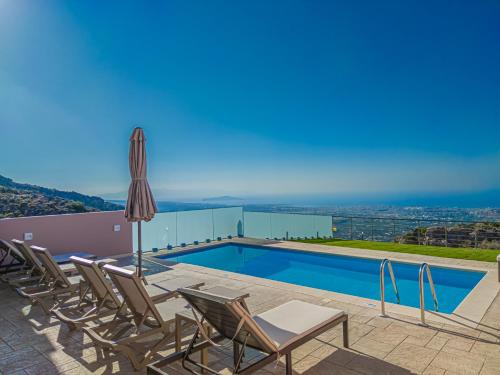 a villa with a swimming pool with chairs and an umbrella at Villa Mari Chania, with private ecologic pool and amazing view! in Chania