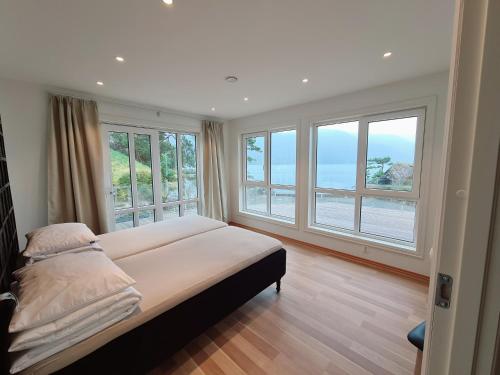 a bedroom with large windows and a bed with white sheets at Ropeid Villa Fjordferie in Ropeid