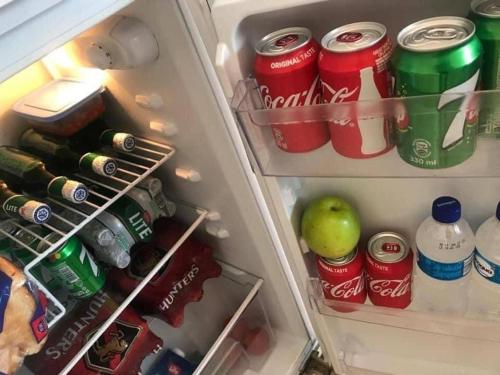 una nevera abierta con latas de refresco y una manzana en ella en The Hawks Bed and Breakfast en Harare