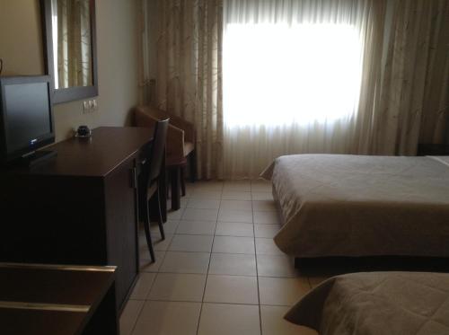 a room with two beds and a desk with a television at Hotel Electra in Volos