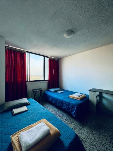 Cette chambre comprend 2 lits, une table et des fenêtres. dans l'établissement Mae's Skate House, à Cali