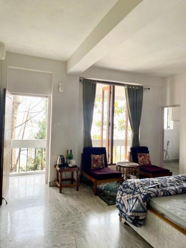 a living room with a bed and chairs and windows at THE GINGKO EYRIE in Kalimpong