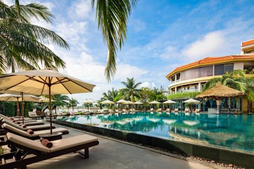 una piscina en el complejo con tumbonas y sombrillas en Bel Marina Hoi An Resort, en Hoi An