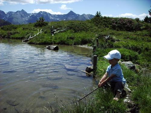 a young boy sitting on the side of a river fishing at Alpenapart Walch in Jerzens