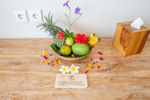 a bowl of fruit and flowers on a table with a card at Green D'mel Bali in Nusa Dua