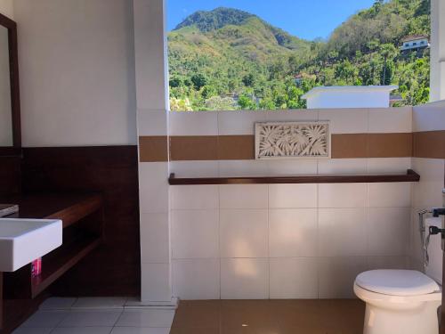 a bathroom with a toilet and a window with mountains at Meditasi Bungalows & Villas in Amed