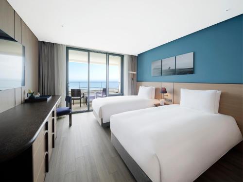 two beds in a hotel room with a view of the ocean at Parnas Hotel Jeju in Seogwipo