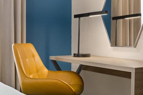 a yellow chair sitting next to a desk with a mirror at Holiday Inn Express & Suites Greenville-Downtown by IHG in Greenville